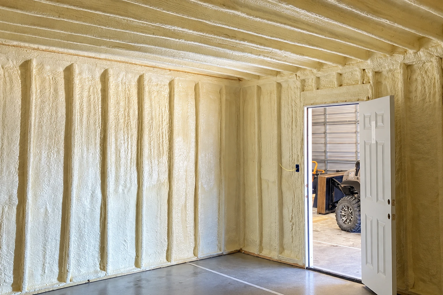 Cream-colored closed-cell spray foam fills the wall and ceiling cavities of a garage.