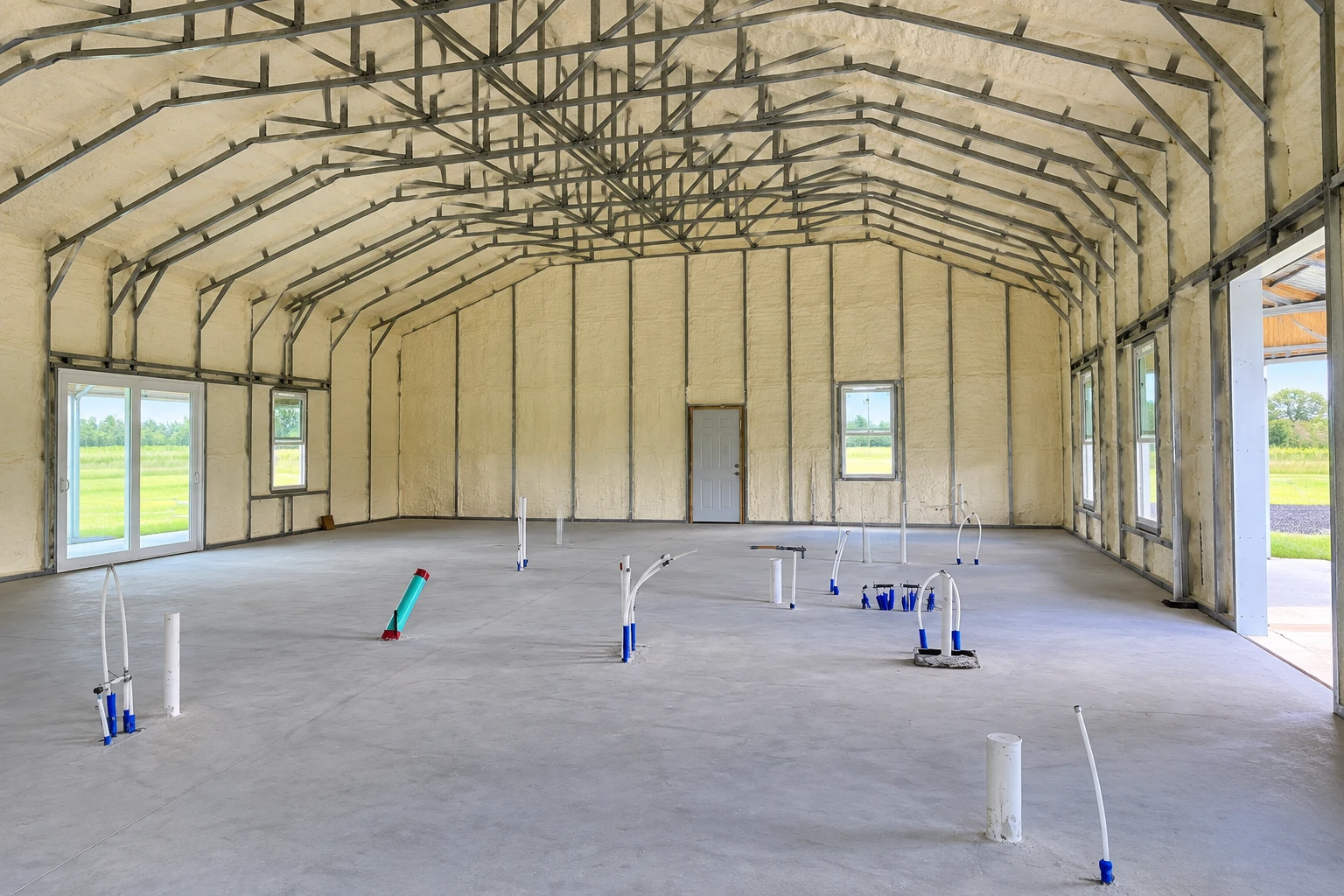 A large commercial building has foam insulation across its walls and roof, with exposed steel framing and a concrete floor.
